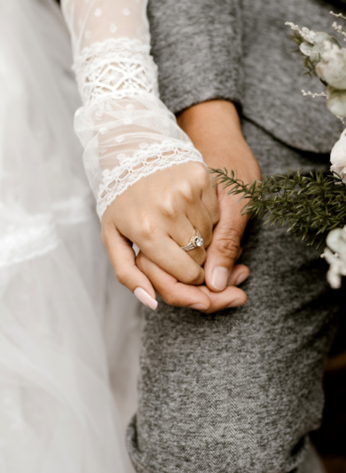Two people holding hands with a woman showing off her wedding ring.