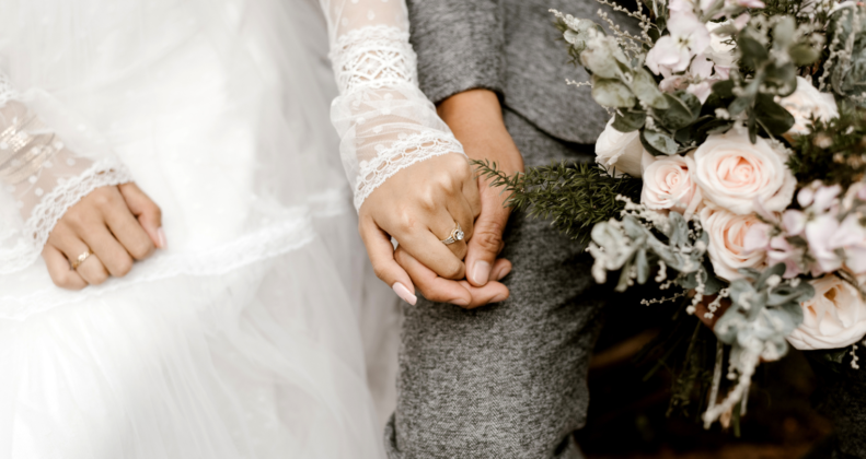 Two people holding hands with a woman showing off her wedding ring.